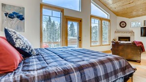 Quarto com uma cama grande, lareira e várias janelas com vista para árvores.