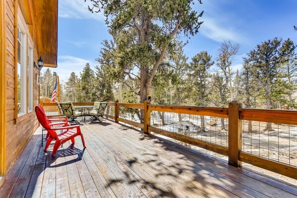 A wooden deck with outdoor furniture, a railing, and a view of trees and a sandy area.