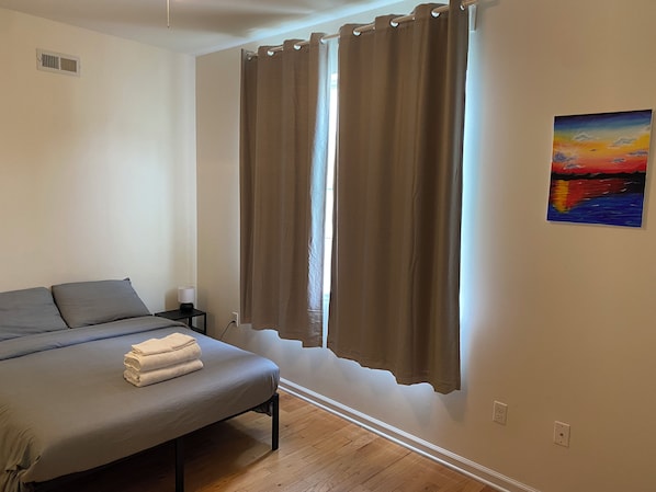 Un dormitorio con cama, mesita de noche, lámpara y un cuadro en la pared.