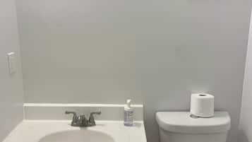 A bathroom with a white sink, wooden cabinets, a toilet, and a framed picture on the wall.