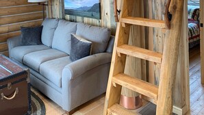 A cozy cabin interior with a wooden interior, a gray sofa, a ladder, and a painting of a landscape. - River Haven Cabin-South-Private River Access! (Emigrant)