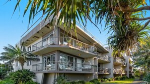 Un hôtel à plusieurs étages doté de balcons, d’une pelouse bien entretenue et de plantes tropicales.