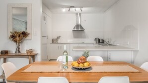Une cuisine moderne avec des armoires blanches, une hotte de cuisinière en acier inoxydable et un petit îlot central doté d’un évier.
