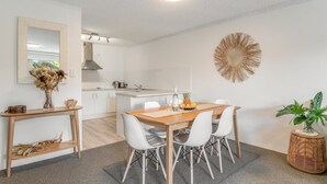 Une cuisine moderne avec des meubles blancs, une table à manger en bois et un grand miroir.