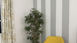 A room with a yellow chair, a small white table, a potted plant, and a striped wall. - Downtown Cosy and Quiet Apartment (Funchal)