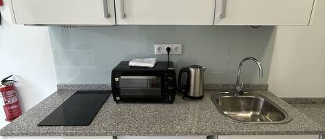 Une cuisine compacte avec des meubles blancs, un four grille-pain noir, un évier en acier inoxydable et un lave-vaisselle blanc.