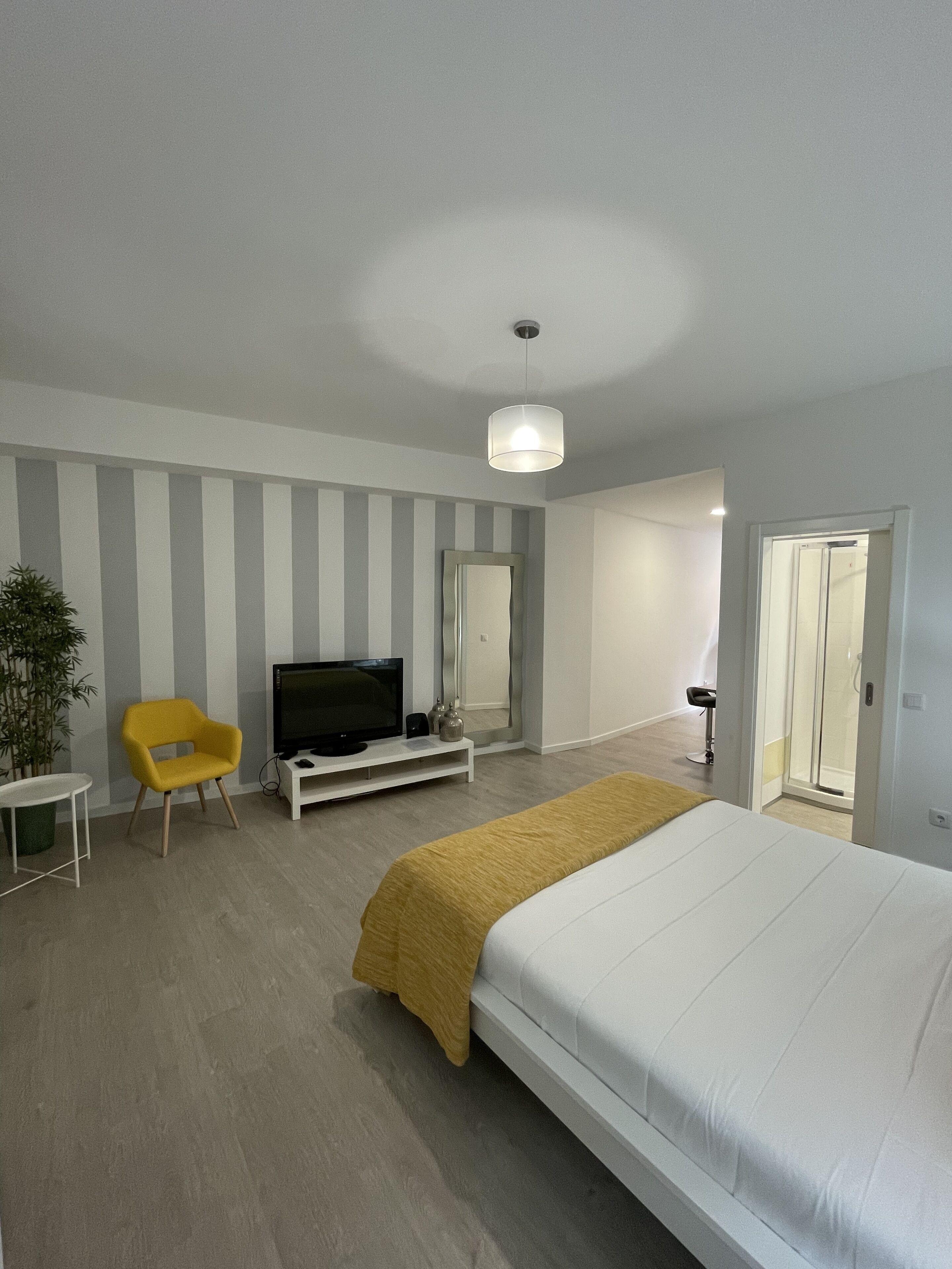 A modern bedroom with a large bed, a television, a yellow chair, and a plant.
