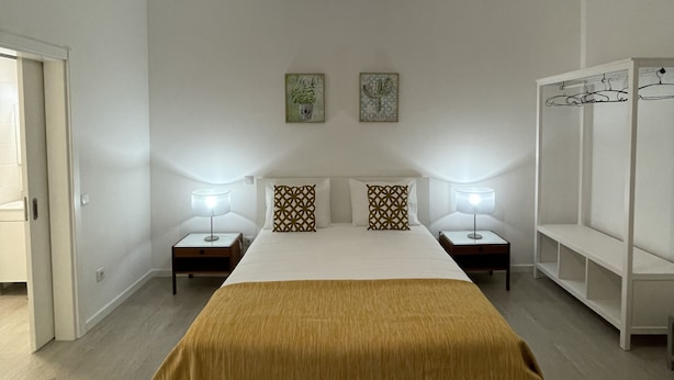 A bedroom with a large bed, two bedside tables with lamps, a wardrobe, and a hanging light fixture. - Downtown Cosy and Quiet Apartment (Funchal)