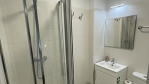 A bathroom with a glass-enclosed shower, a sink, a toilet, and a mirror. - Downtown Cosy and Quiet Apartment (Funchal)