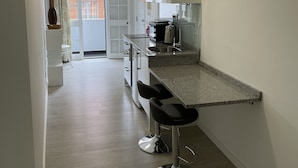 A modern kitchen with a granite countertop, two bar stools, and a view of the outside. - Downtown Cosy and Quiet Apartment (Funchal)