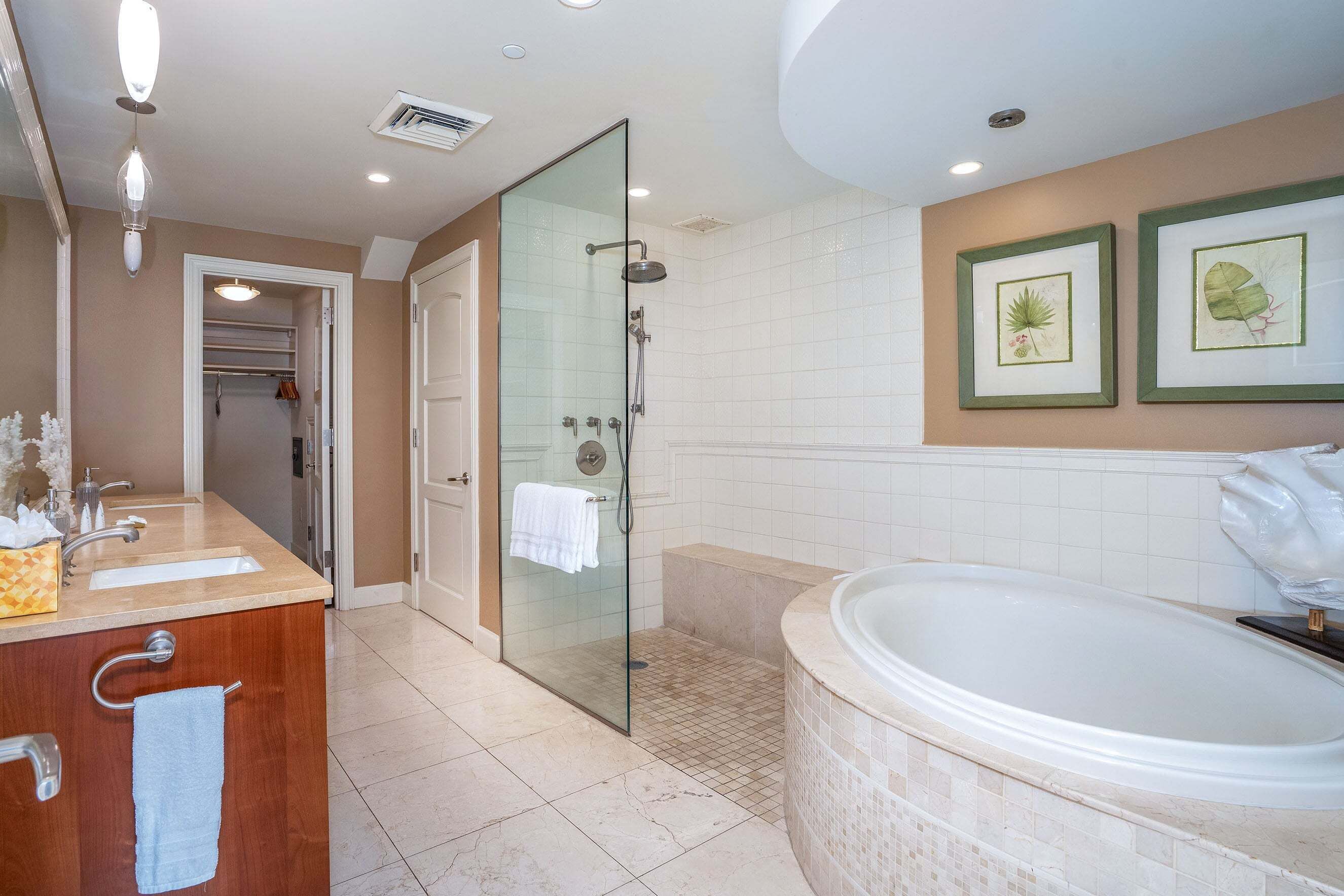 A bathroom with a glass-enclosed shower, a large bathtub, a vanity with a mirror, and two framed botanical prints on the wall.