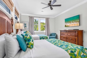 Une chambre d’hôtel avec un lit, une chaise, une commode, un ventilateur de plafond et un tableau accroché au mur.