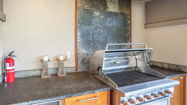 A kitchen with a built-in grill, a fire extinguisher, and two candles on the counter. - Luxurious Ho'olei 12-2, Lush View, Close to Pool, Sleeps 8 in beds, Central AC! (Kihei)