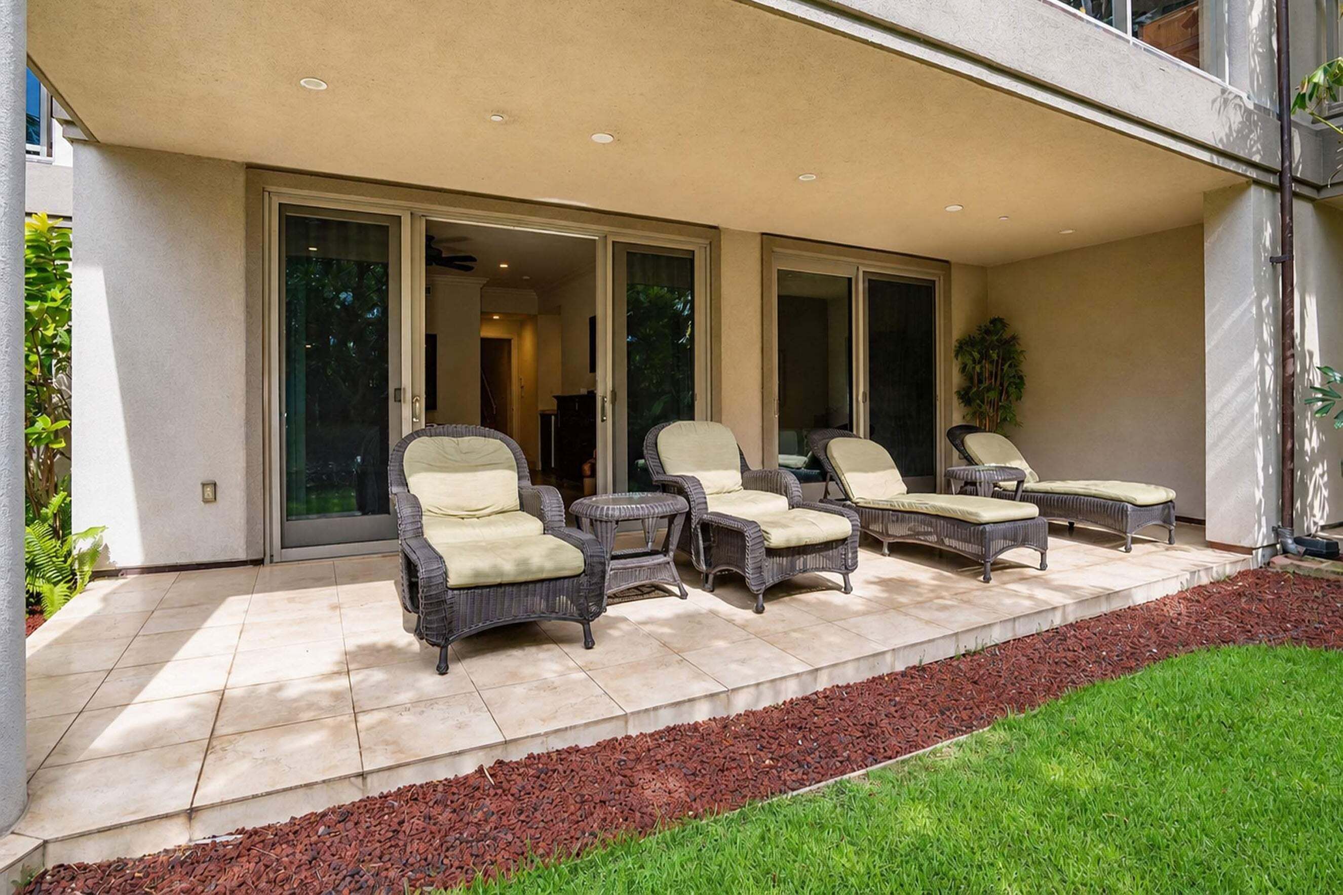 A covered patio with wicker furniture and a well-maintained lawn.