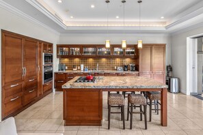 A spacious kitchen with wooden cabinets, a granite countertop, and a central island with bar stools. - Luxurious Ho'olei 12-2, Lush View, Close to Pool, Sleeps 8 in beds, Central AC! (Kihei)
