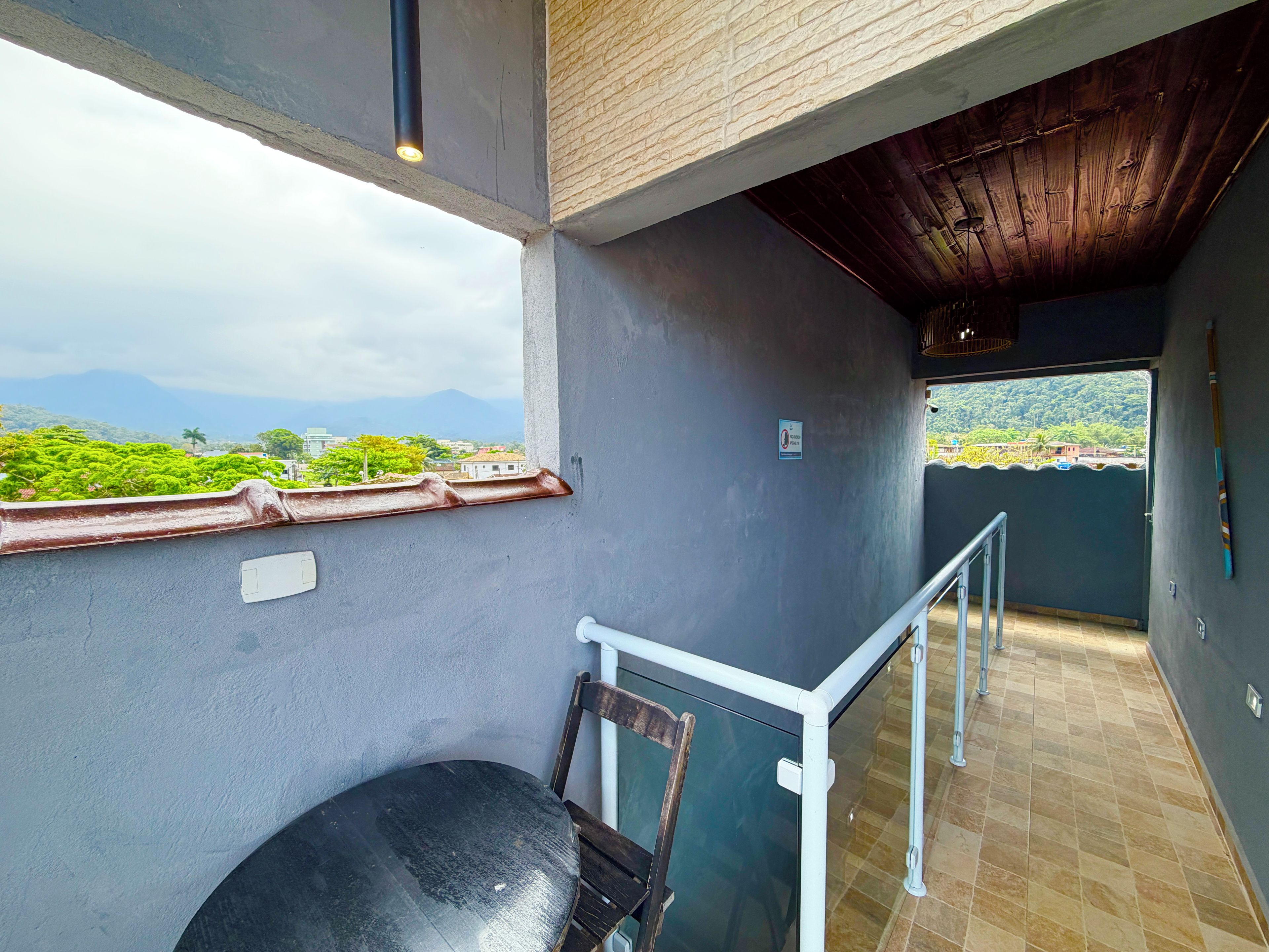 Un balcón con vistas a zonas verdes y montañas, una silla y una barandilla.