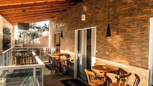Un restaurante con terraza, mesas y sillas de madera, un muro de piedra y una barandilla de vidrio.