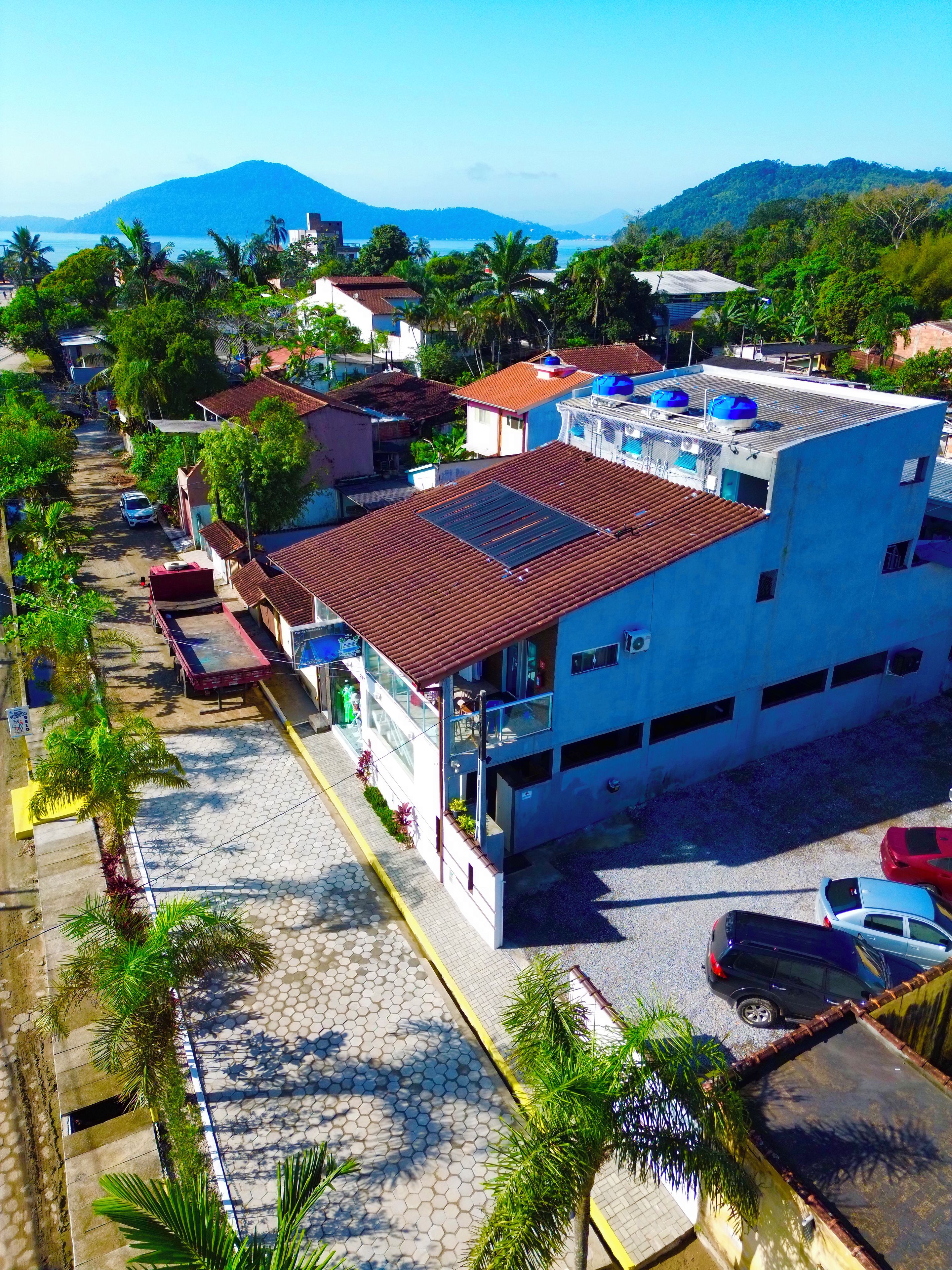 Un edificio de varios pisos con techo plano, rodeado de un área pavimentada con coches estacionados y palmeras.