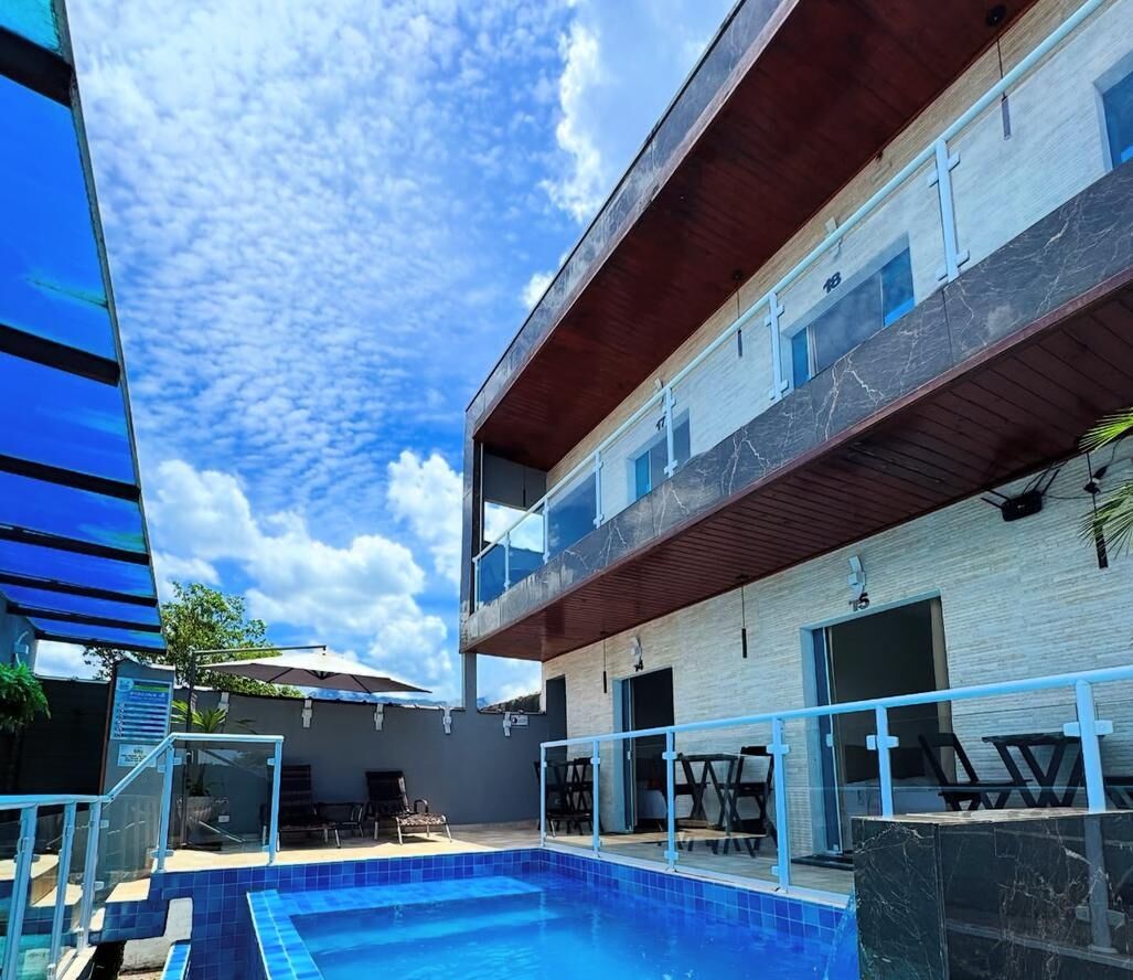 Un edificio de dos pisos con piscina, zona de estar exterior y cielo azul despejado.