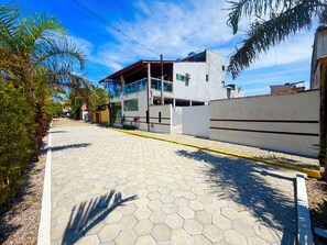 A paved pathway leading to a modern building with a glass balcony, surrounded by greenery.