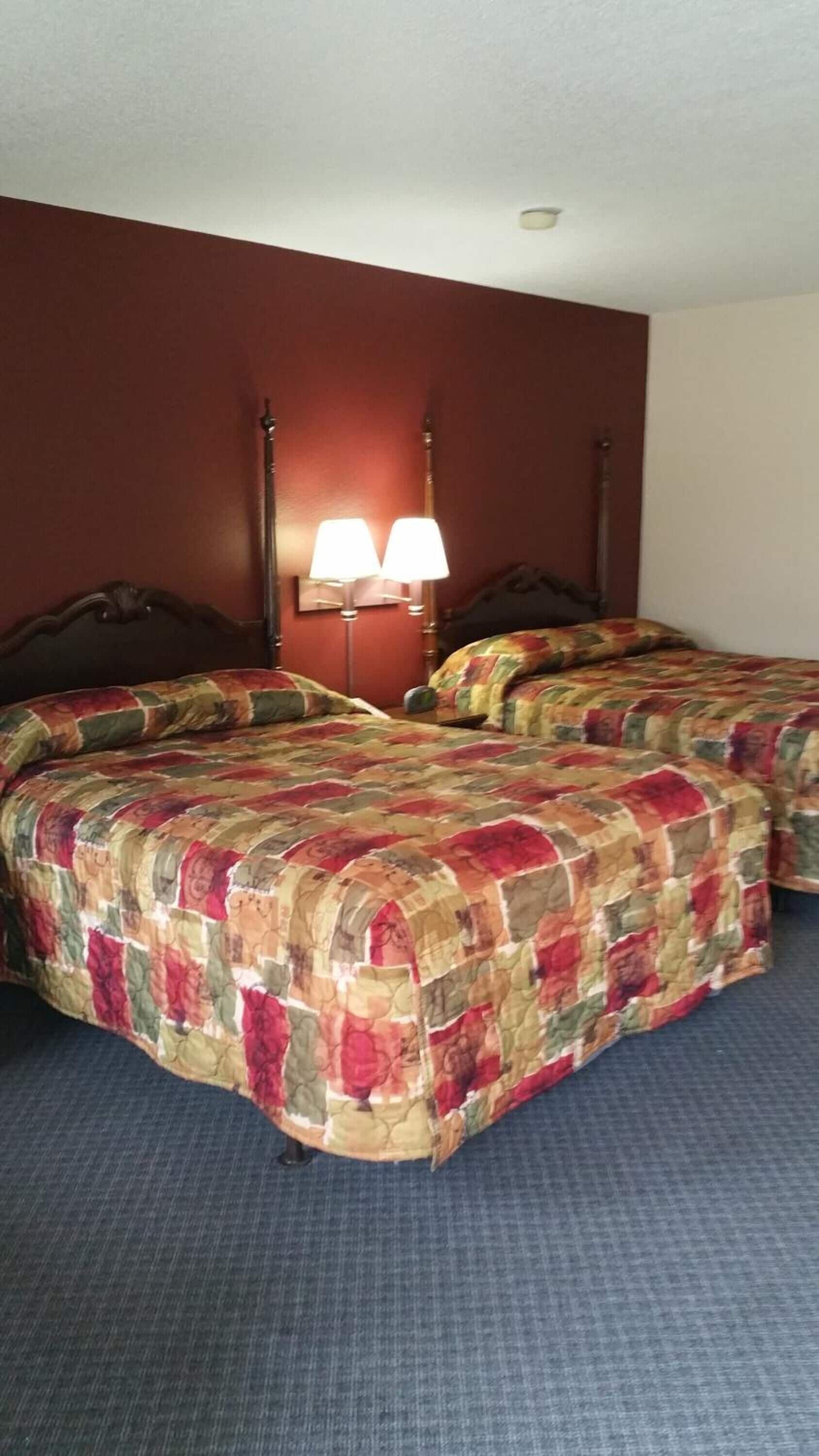 A hotel room with two beds, each with a floral-patterned bedspread, a nightstand with a lamp, and a dark wooden headboard.