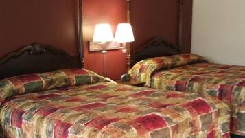 A hotel room with two beds, each with a floral-patterned bedspread, a nightstand with a lamp, and a dark wooden headboard.