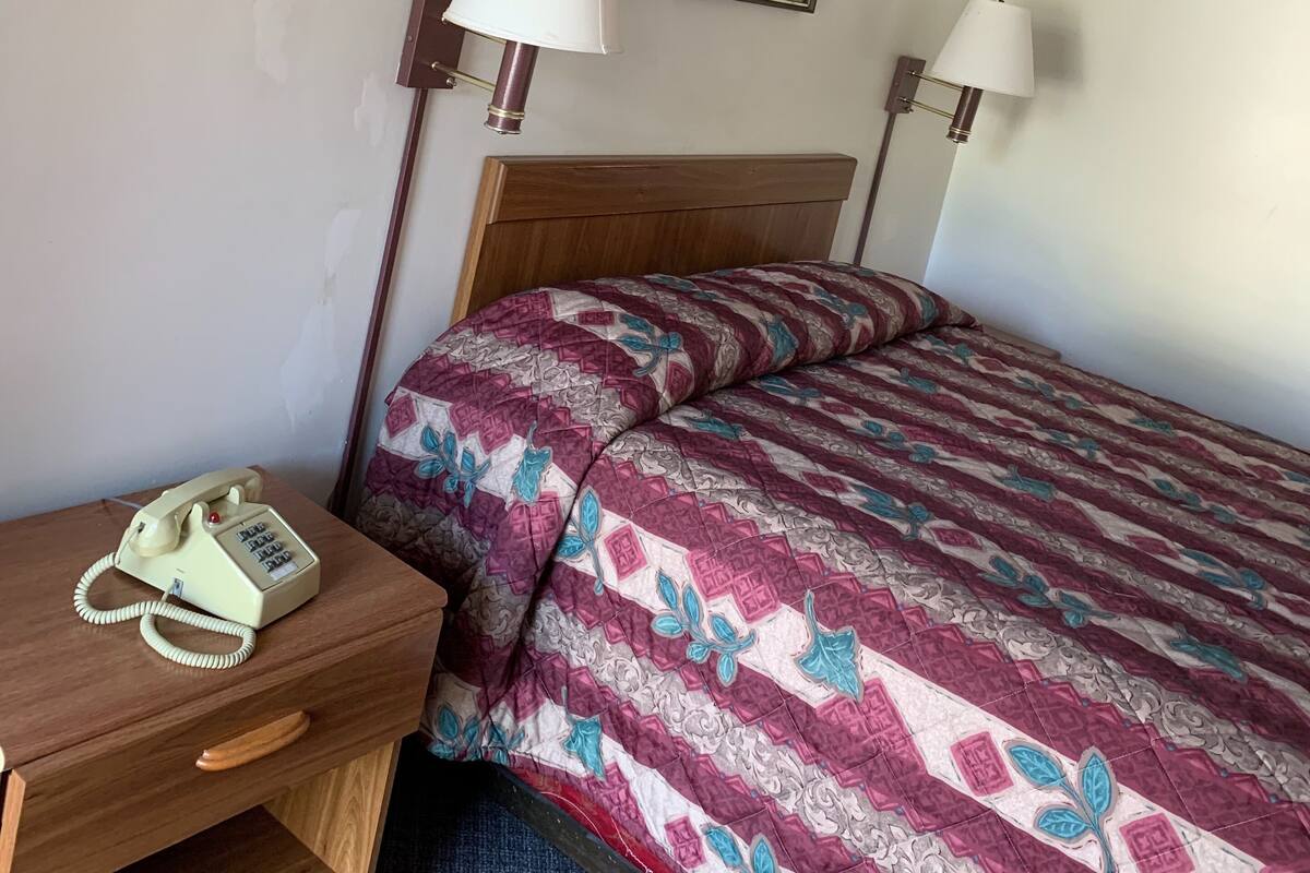 A hotel room with a bed, a desk with a telephone, and two wall-mounted lamps.