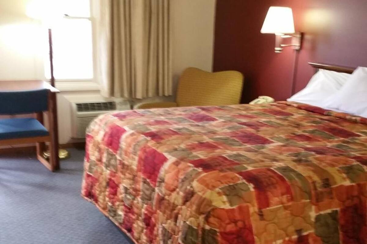 A hotel room with a bed, a chair, a lamp, and a window with curtains.