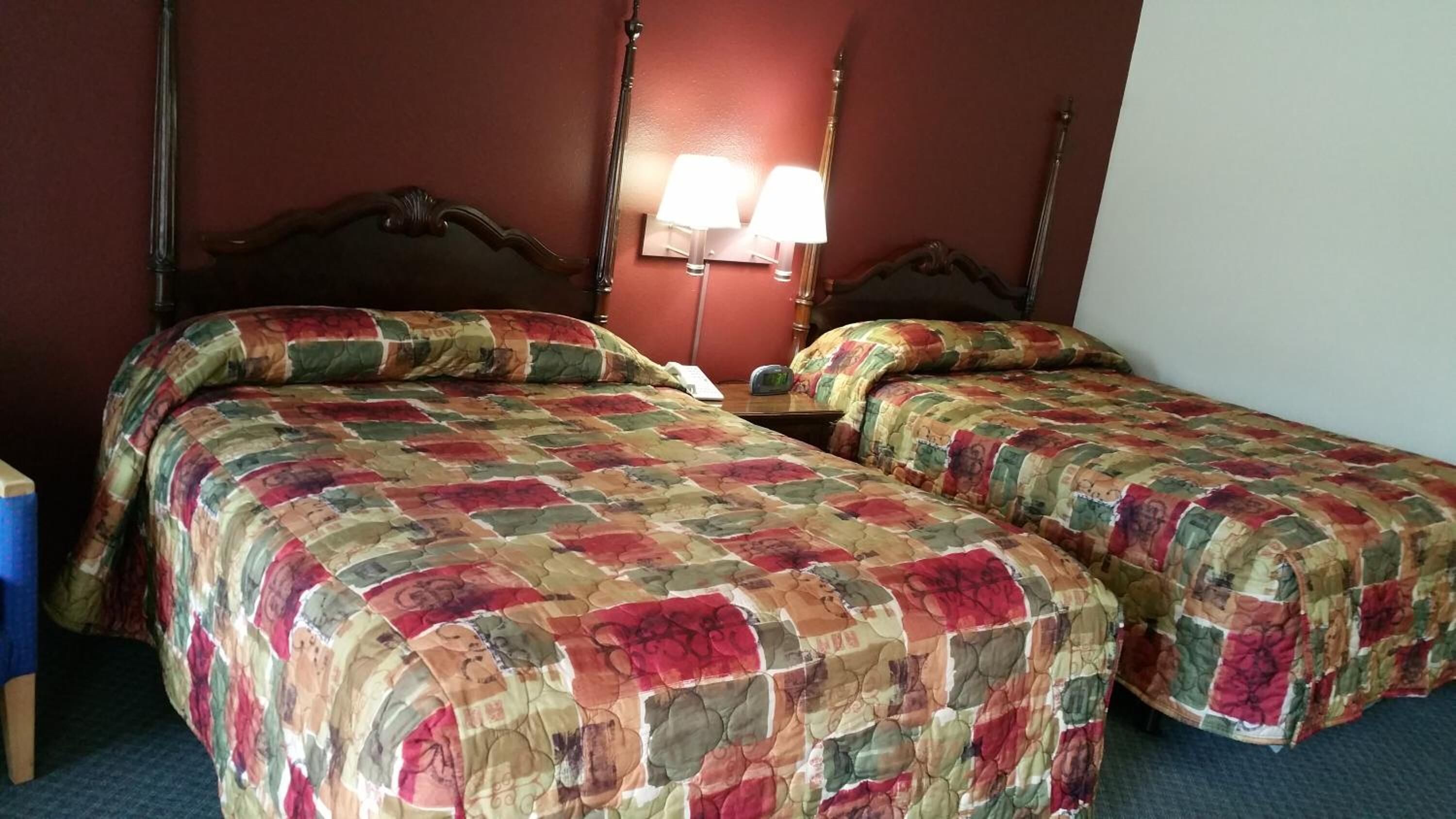 Habitación de hotel con dos camas, cada una con colcha de motivos florales, una mesita de noche con lámpara y cabecero de madera.