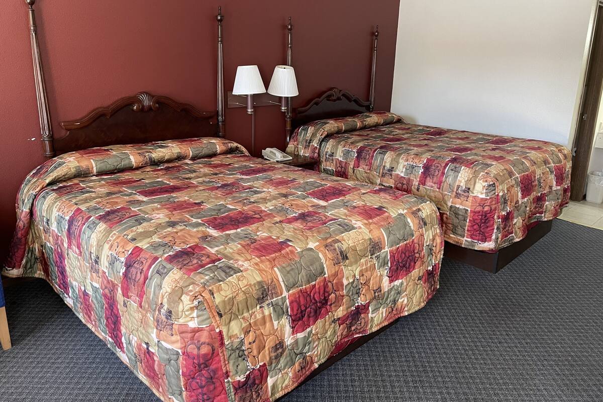 A double bed with a floral quilt, a bedside table with a lamp, and a wooden headboard.