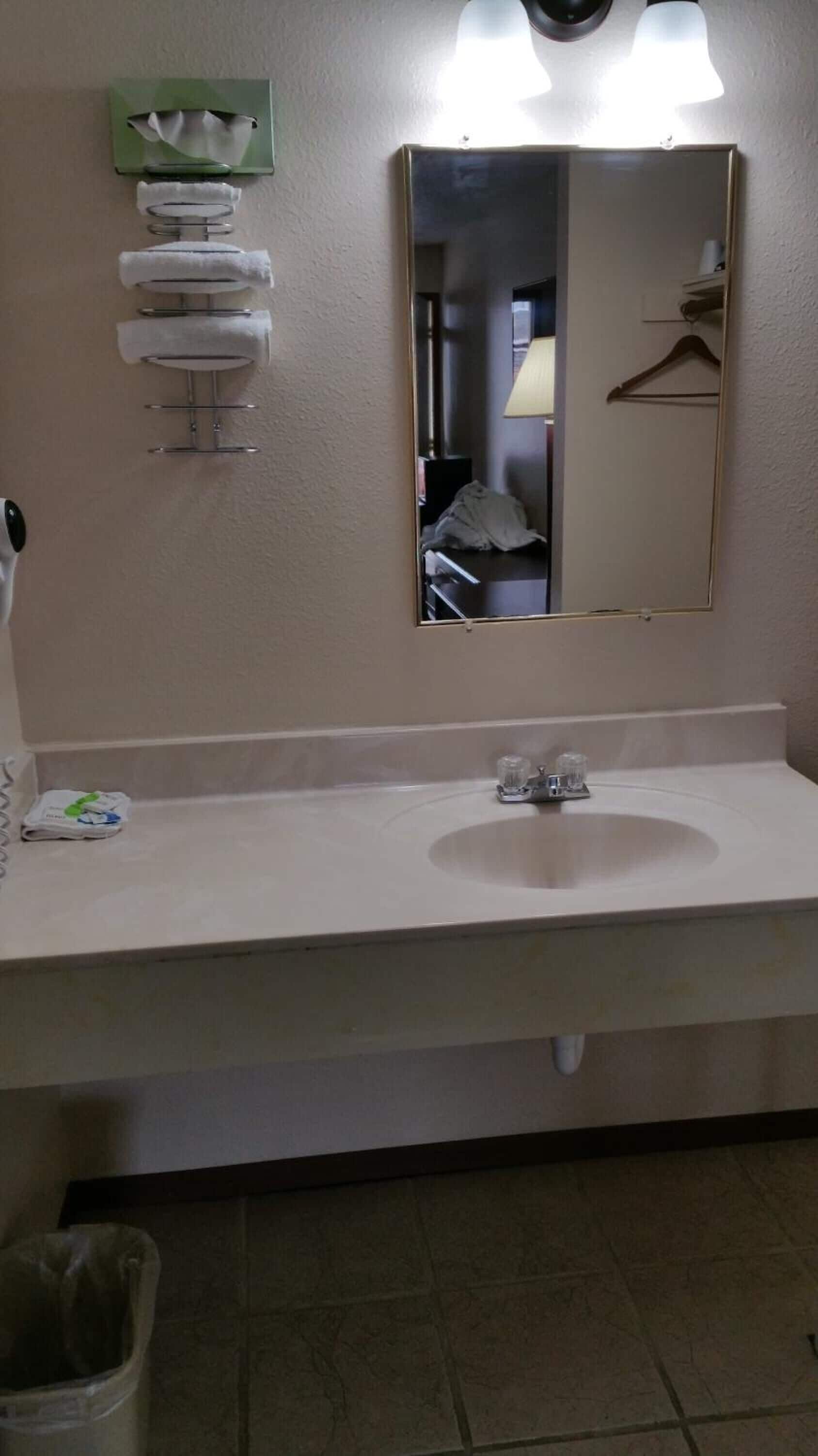 A bathroom with a white sink, a mirror, and a towel dispenser.