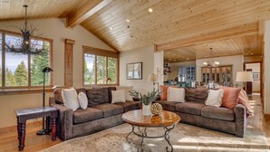 A spacious living room with a large brown sectional sofa, a round coffee table, and a wooden ceiling. - Home Run at Northstar - TLUXP (Truckee)