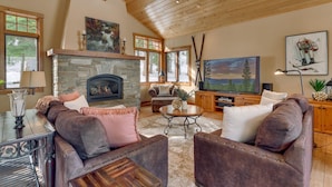 A cozy living room with a stone fireplace, leather sofas, a flat-screen TV, and a large window. - Home Run at Northstar - TLUXP (Truckee)