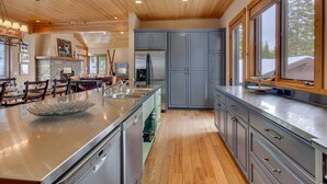 A modern kitchen with wooden ceiling, grey cabinets, stainless steel appliances, and a large island with a glass bowl. - Home Run at Northstar - TLUXP (Truckee)
