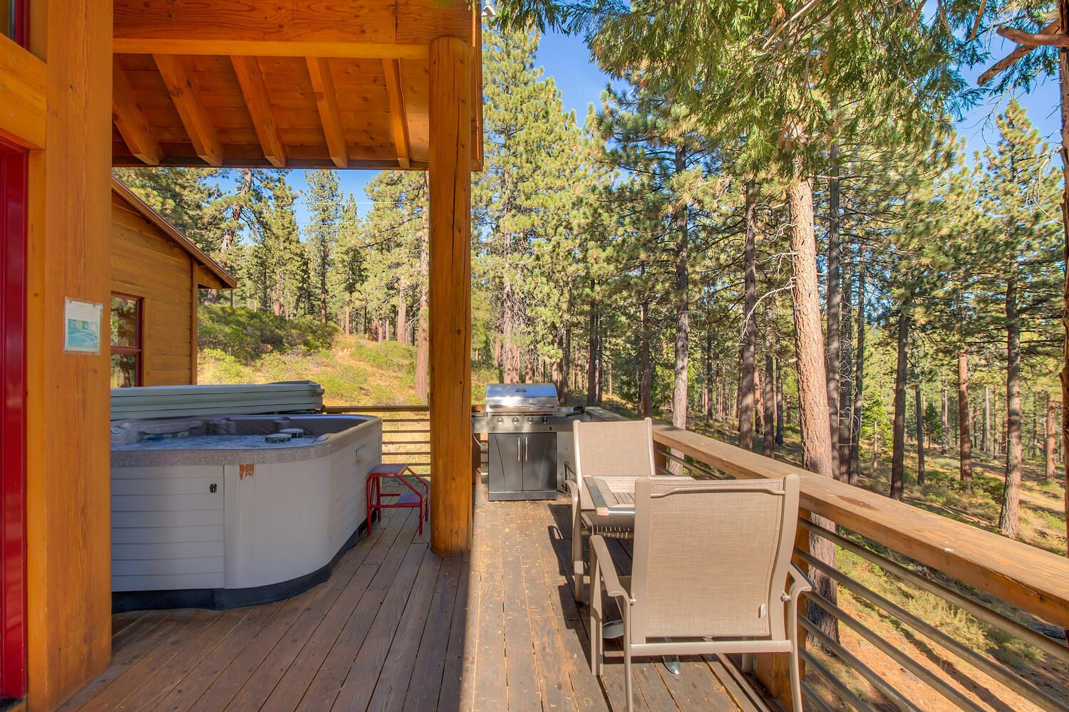 Una terraza de madera con jacuzzi, parrilla y zona de estar al aire libre, con vistas a un bosque.