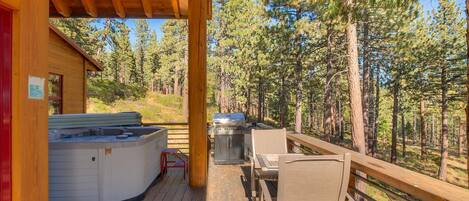 Una terraza de madera con jacuzzi, parrilla y zona de estar al aire libre, con vistas a un bosque.