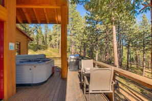 Relax on the deck with a hot tub and grill, surrounded by a serene forest setting.