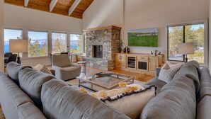 Un salón espacioso con chimenea de piedra, ventanas amplias y un alto techo de madera.