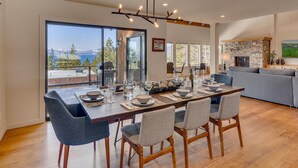 Un moderno comedor con una mesa grande dispuesta para cuatro personas, una chimenea de piedra y vistas al exterior.