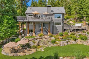 A two-story house with a balcony, a stone patio, and a grassy lawn.