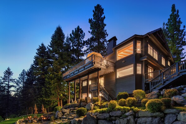 A multi-level house with a deck, surrounded by trees and a landscaped garden.