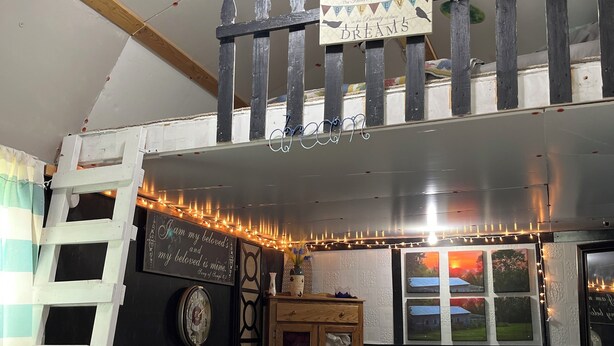 A cozy room with a loft bed, a desk, a ladder, and a window with a view of a house. - Glamping at Peace In The Valley (Glasgow)
