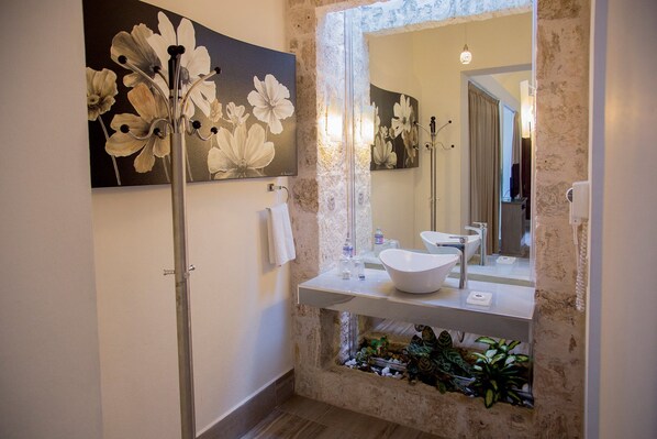 Un baño con un espejo grande, un lavabo blanco y una ducha. Hay un cuadro de flores en la pared y una planta en el suelo.