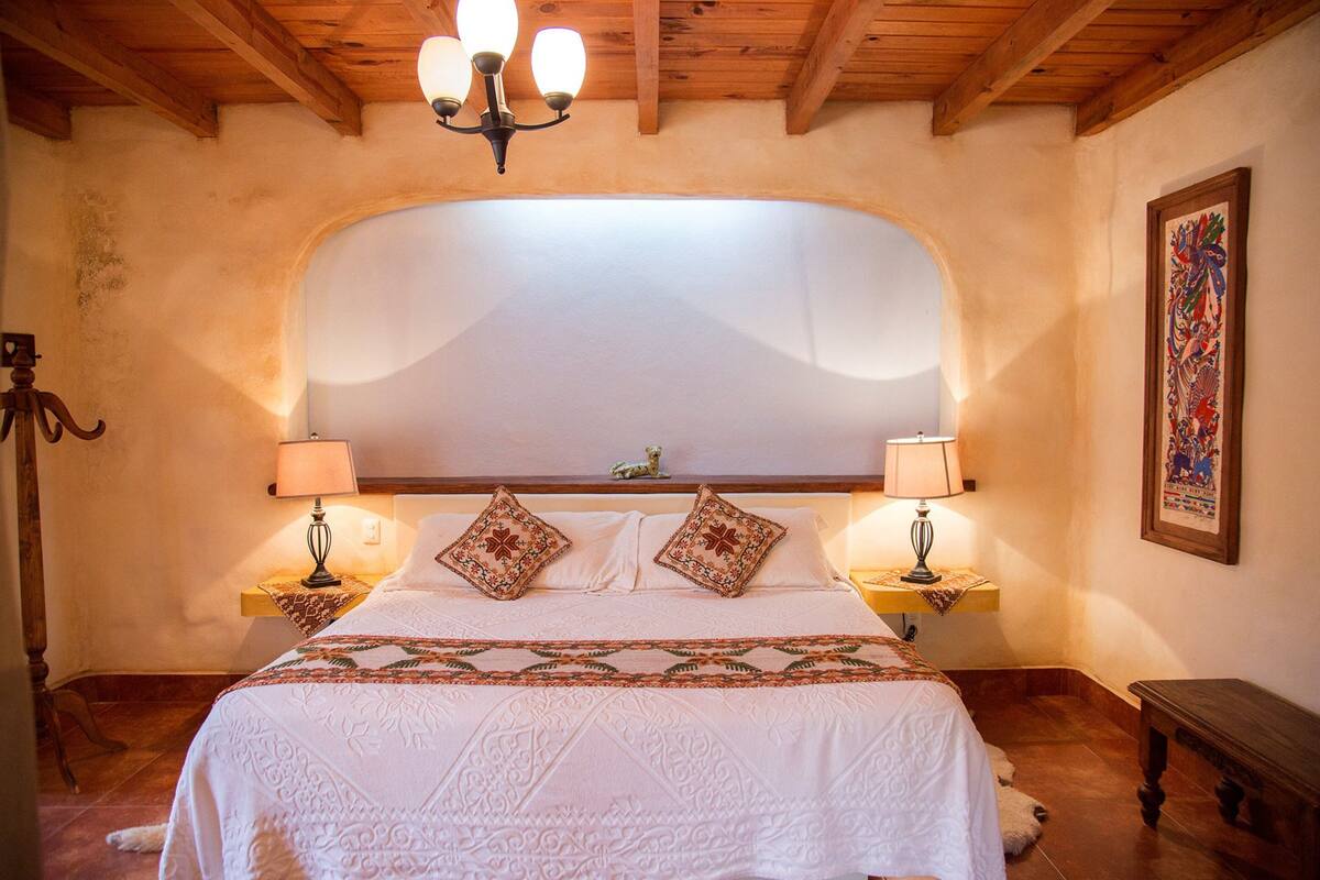 A bedroom with a large bed, two bedside lamps, a wooden headboard, and a decorative wall piece.