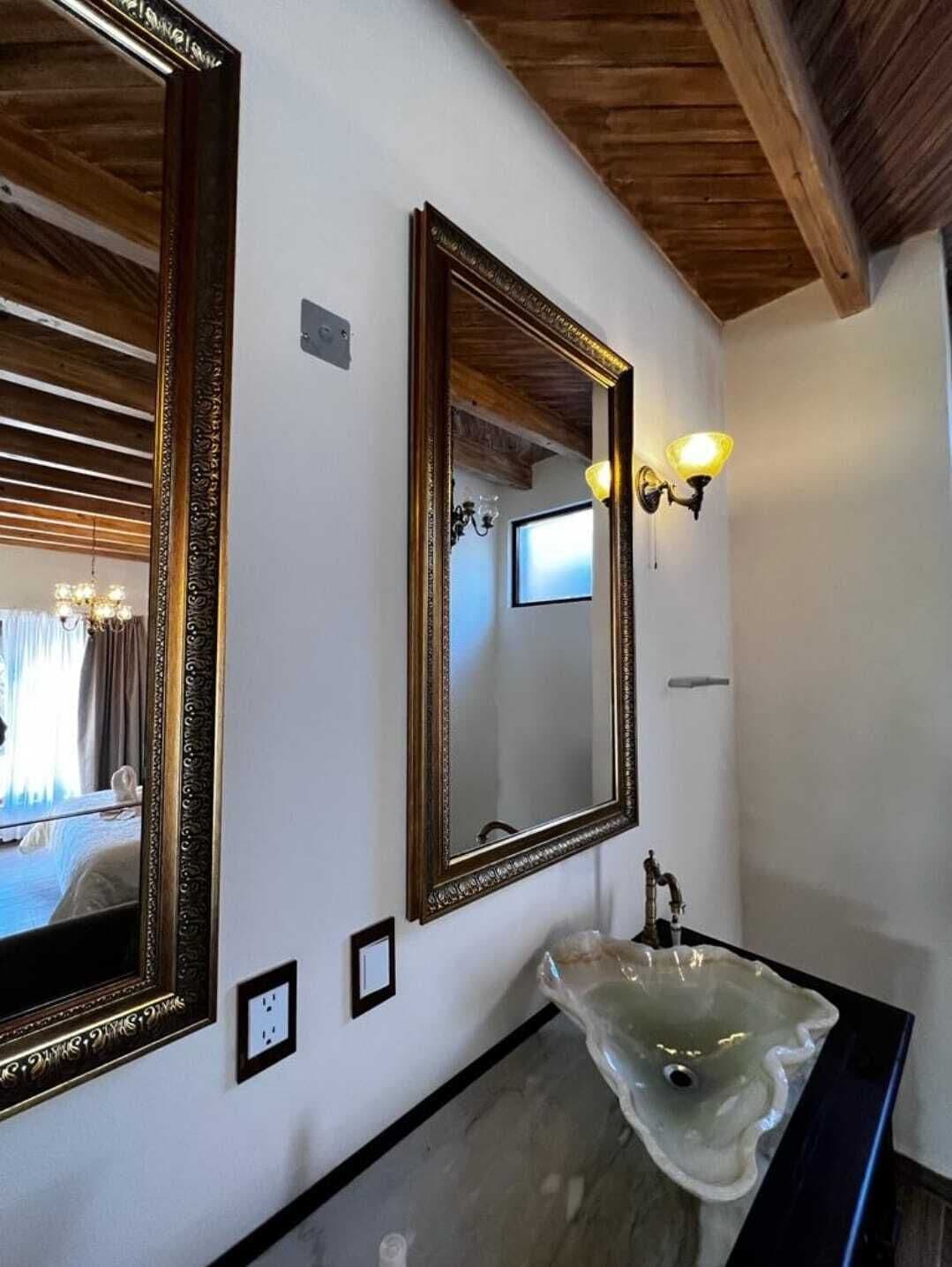 Un baño con dos espejos decorados, un lavamanos moderno y una araña.