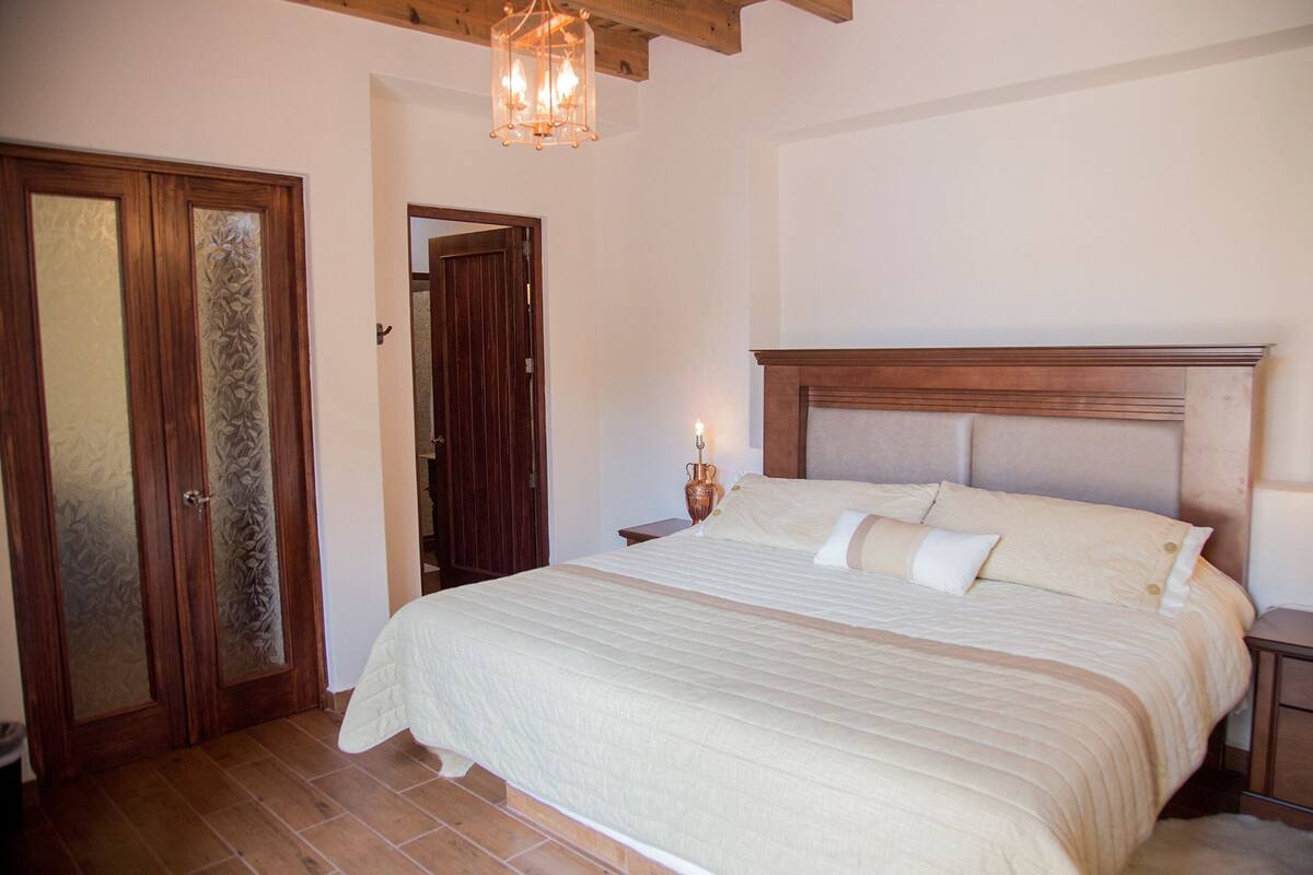 A bedroom with a large bed, wooden headboard, and a nightstand with a lamp.