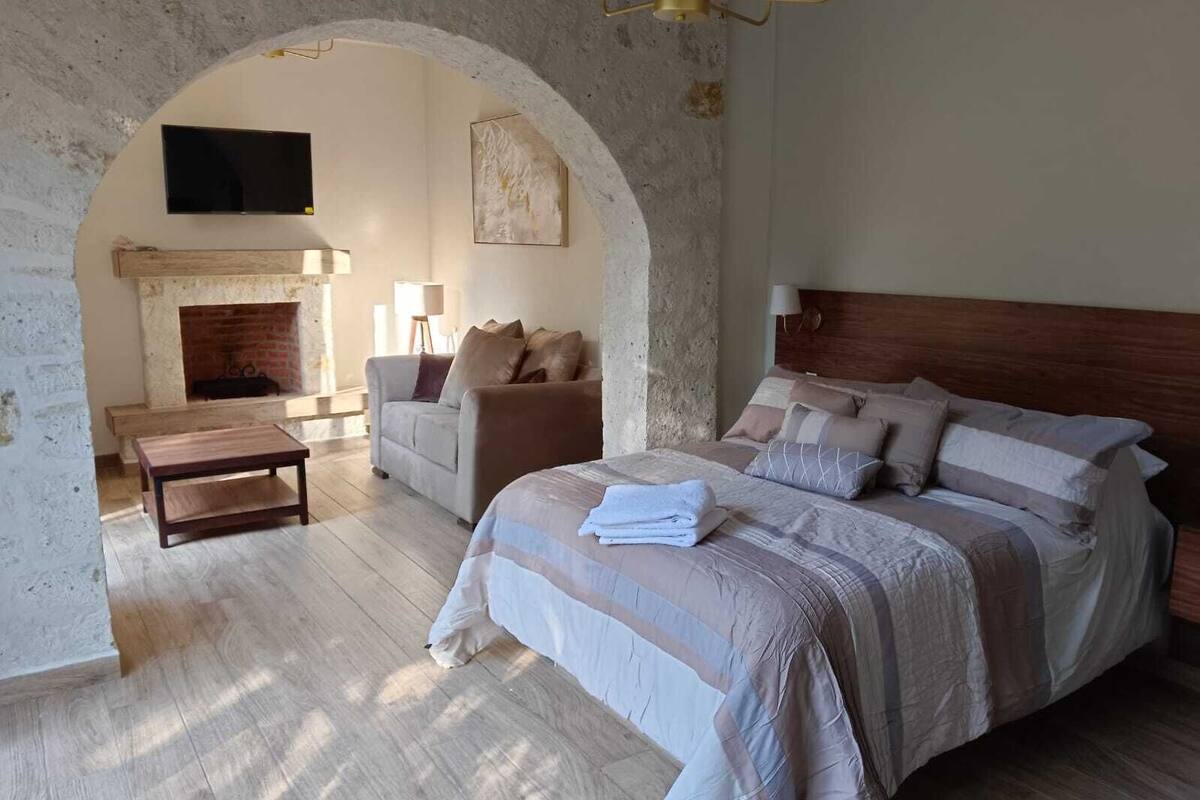 A bedroom with a large bed, a sofa, a coffee table, and a fireplace.