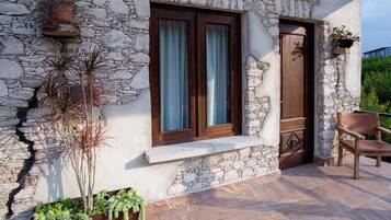 A stone building with a wooden door and window, a bench, and potted plants.