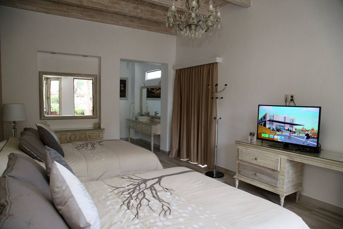 A bedroom with a bed, a television, a dresser, a mirror, and a chandelier.