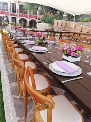 A long dining table set with chairs, floral centerpieces, and a tent overhead. - Hotel Centenario Los Arroyitos (Ezequiel Montes)